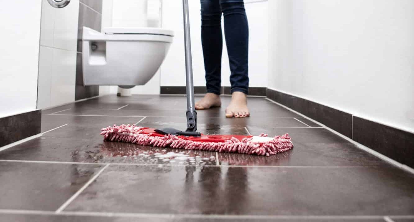 Persoon die vloer van badkamer schoonmaakt met dweil - Hoe toilet schoonmaken: vloer | Asenso Schoonmaakdiensten