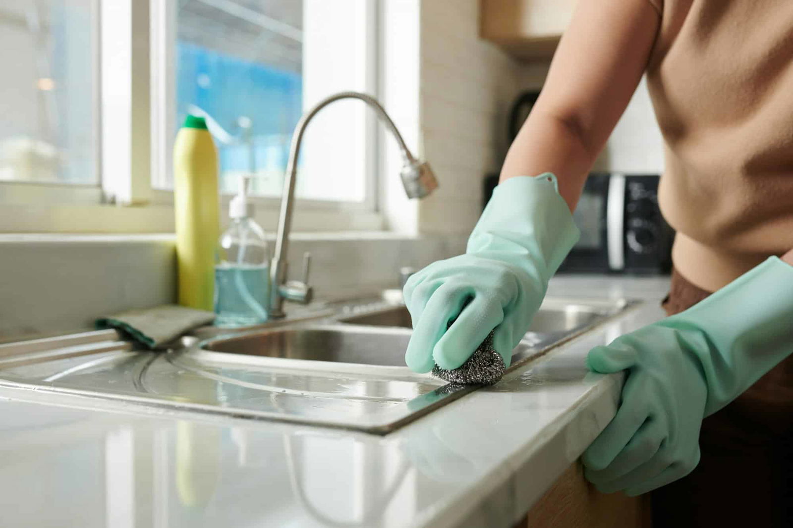 Vrouw die gootsteen schoonmaakt - hoe gootsteen schoonmaken | Asenso Schoonmaakdiensten