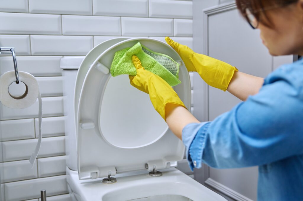 Vrouw die onderkant wc bril schoonmaakt | hoe vaak badkamer schoonmaken | Asenso Schoonmaakdiensten