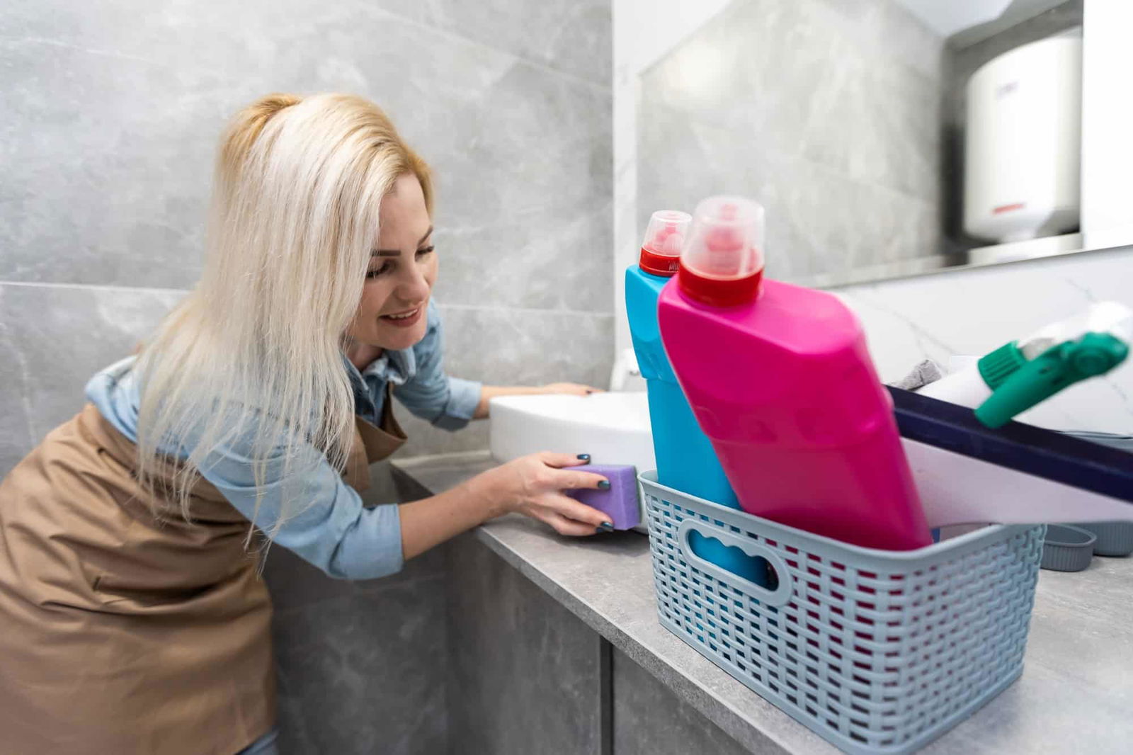 Blonde vrouw die badkamer schoonmaakt | hoe vaak badkamer schoonmaken | Asenso Schoonmaakdiensten