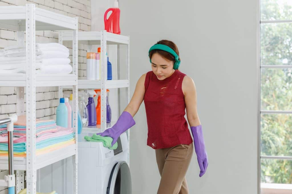 Vrouw luistert naar muziek met een koptelefoon en reinigt de wasmachine in de wasruimte | Hoe wasmachine schoonmaken | Asenso Schoonmaakdiensten