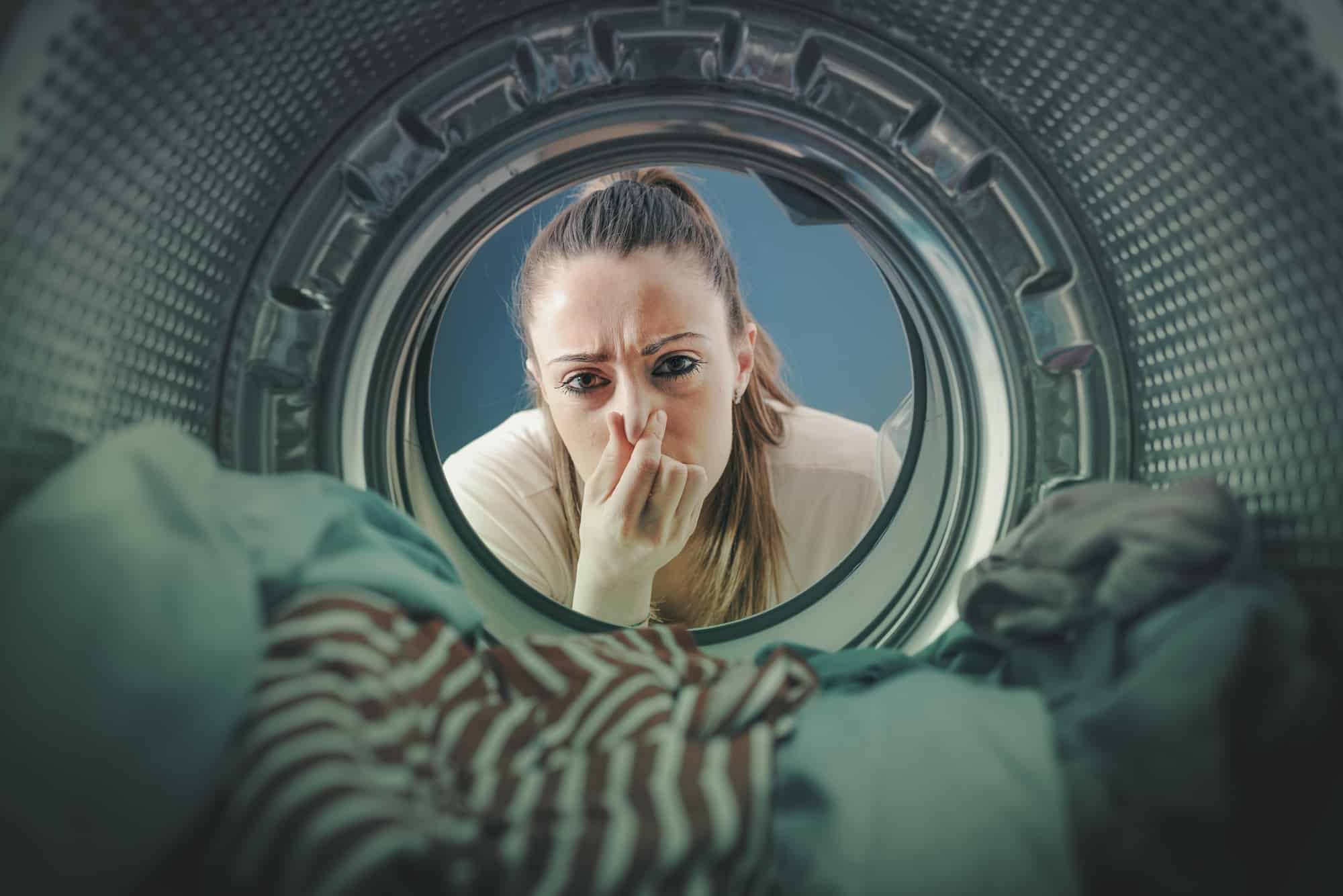 Vrouw die neus dichtknijpt vanuit stinkende wasmachine gezien | Hoe wasmachine schoonmaken | Asenso Schoonmaakdiensten
