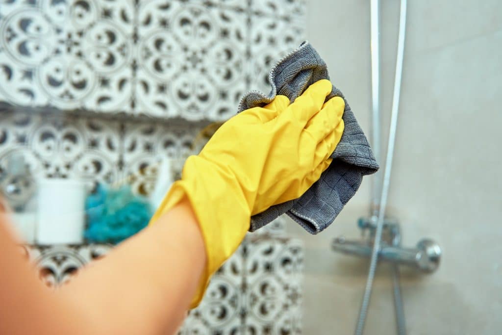 Hand met handschoen die douchecabine schoonmaakt | Hoe badkamer schoonmaken | Asenso Schoonmaakdiensten