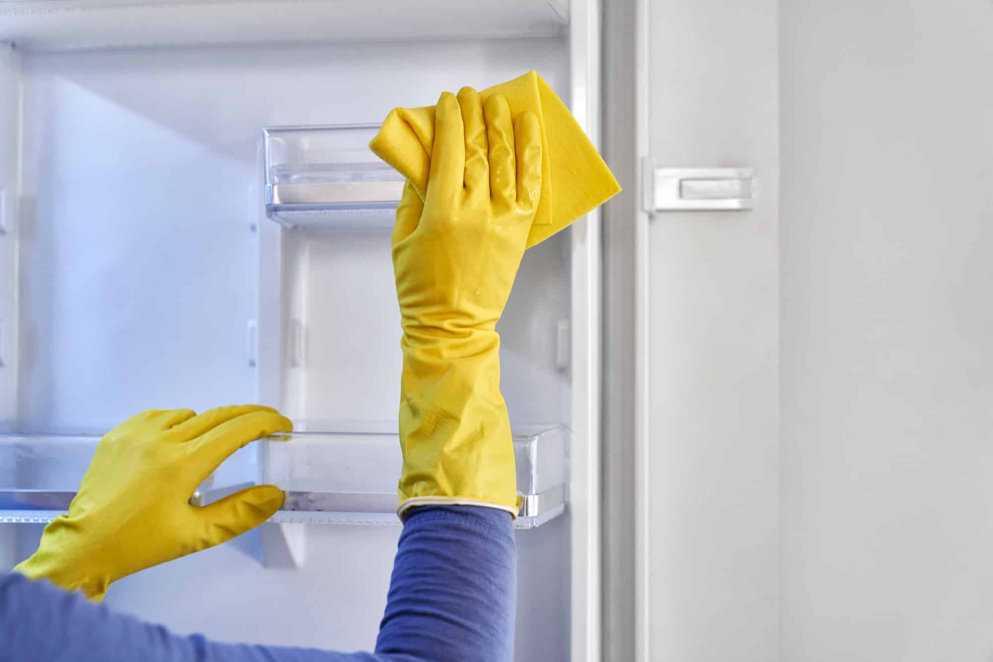 Persoon met gele handschoenen die koelkast schoonmaakt | Hoe koelkast schoonmaken | Asenso Schoonmaakdiensten