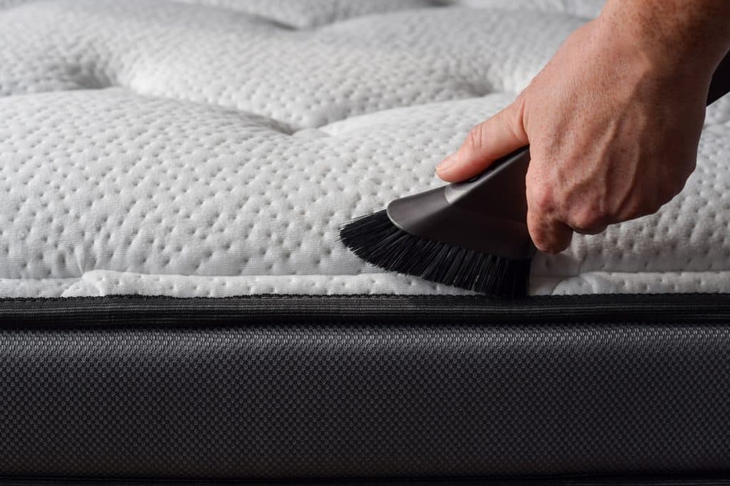 Close-up van hand van een persoon die stofzuiger gebruikt om een matras te stofzuigen | Hoe matras schoonmaken | Asenso Schoonmaakdiensten