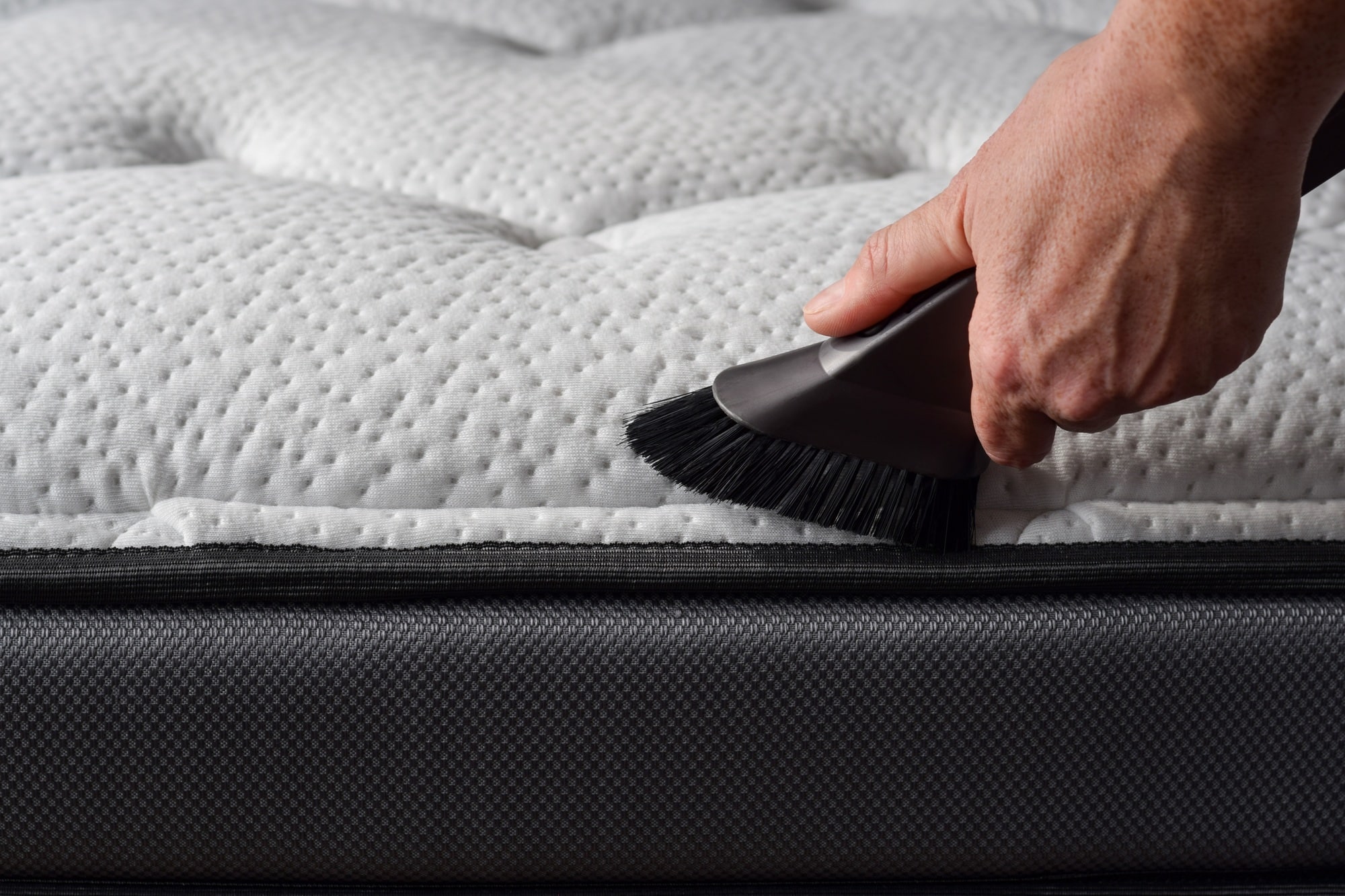 Close-up van hand van een persoon die stofzuiger gebruikt om een matras te stofzuigen | Hoe matras schoonmaken | Asenso Schoonmaakdiensten
