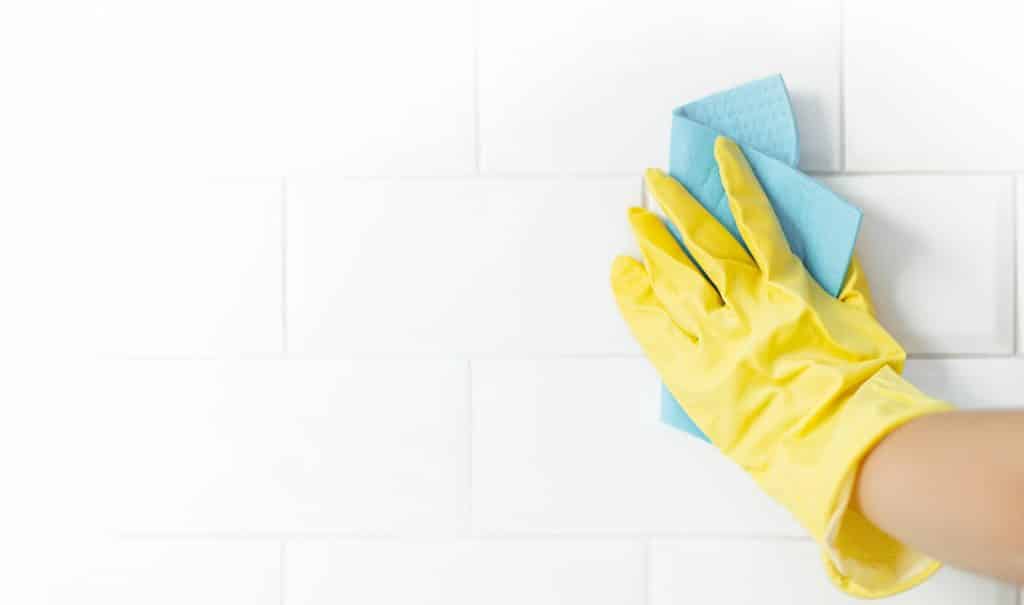 Hand in gele handschoen die voegen schoonmaakt in badkamer | Hoe schimmel badkamer schoonmaken | Asenso Schoonmaakdiensten