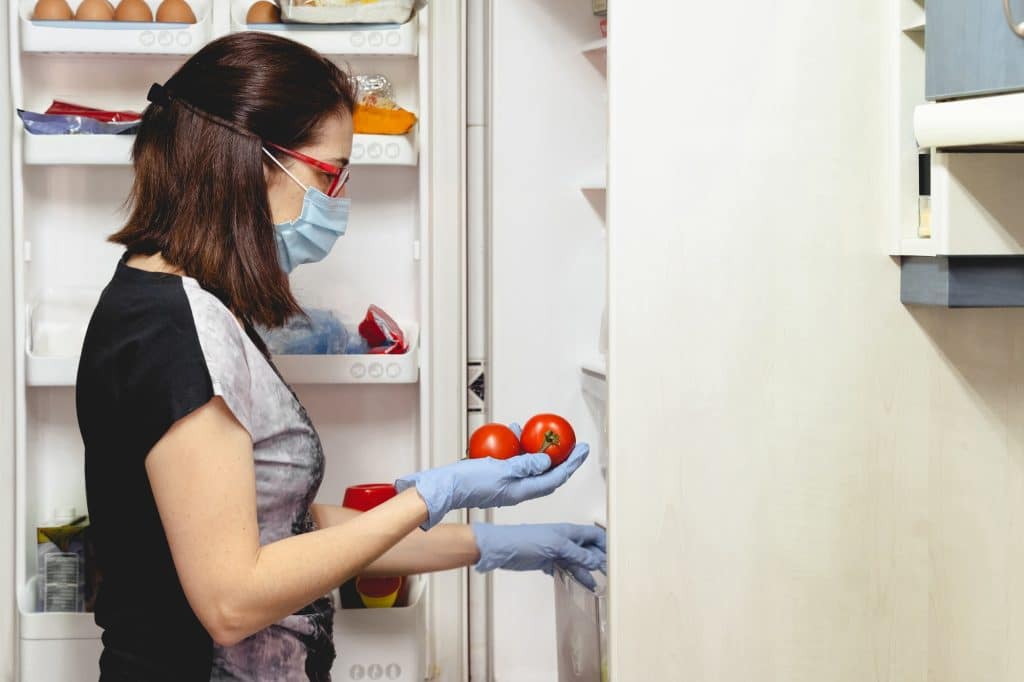 Vrouw met masker en handschoenen die koelkast schoonmaakt | Hoe koelkast schoonmaken | Asenso Schoonmaakdiensten