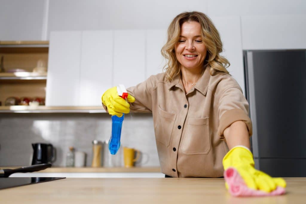 Blonde vrouw met handschoenen die keuken schoonmaakt | Schoonmaakbedrijf particulieren | Asenso Schoonmaakdiensten
