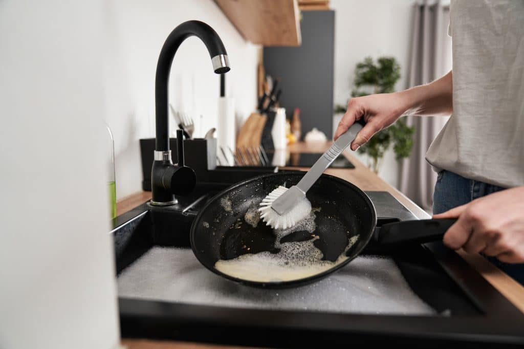 Iemand die pan weekt en schoonmaakt | Aangebrande pan schoonmaken | Asenso Schoonmaakdiensten