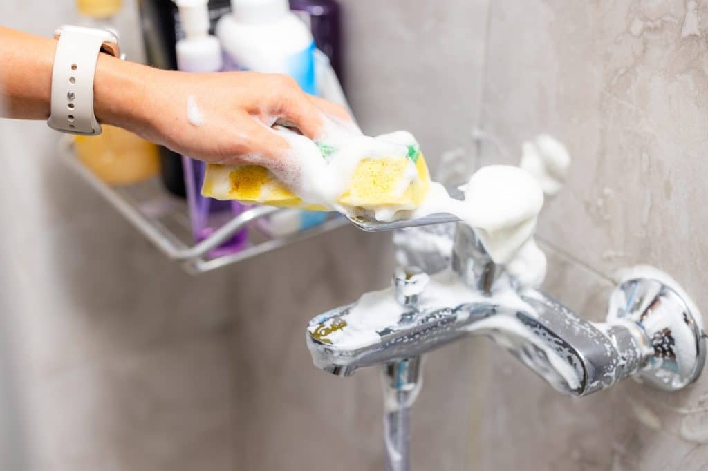 Close-up van hand die kalkvlekken schoonmaakt in badkamer | Kalk schoonmaken | Asenso Schoonmaakdiensten