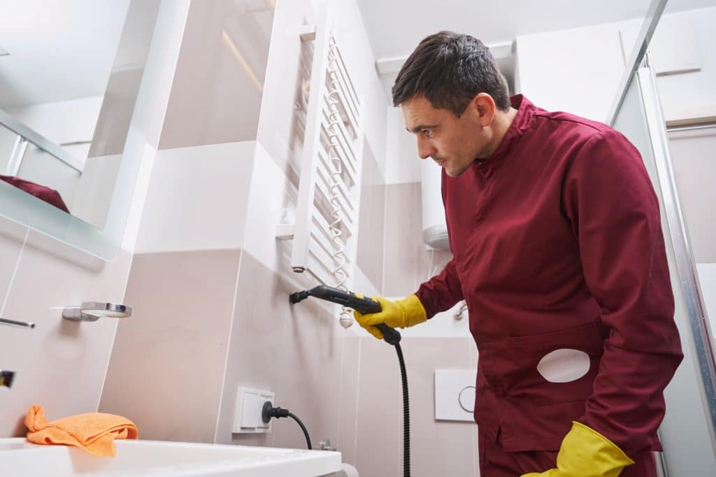 Professionele schoonmaker die met stoom voegen van de badkamer muren schoonmaakt | Badkamer voegen schoonmaken | Asenso Schoonmaakdiensten