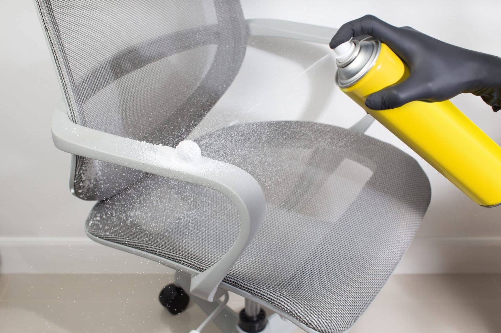 Close-up van schoonmaker die bureaustoel schoonmaakt met spray | Hoe bureaustoel schoonmaken | Asenso Schoonmaakdiensten