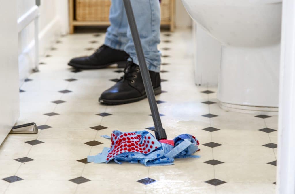 Man die vloertegels dweilt van badkamer | Vloertegels schoonmaken | Asenso Schoonmaakdiensten