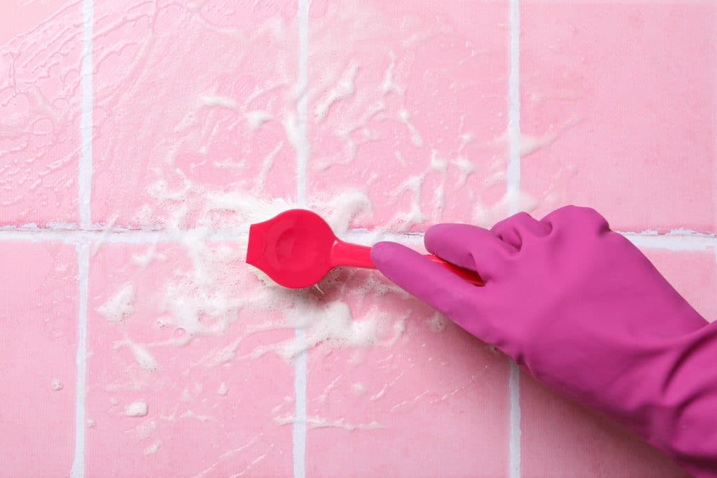 Hand met roze rubberen handschoen die met een sopje en een afwasborstel de tegelvoegen van de keuken schoonmaakt | Tegelvoegen keuken schoonmaken | Asenso Schoonmaakdiensten