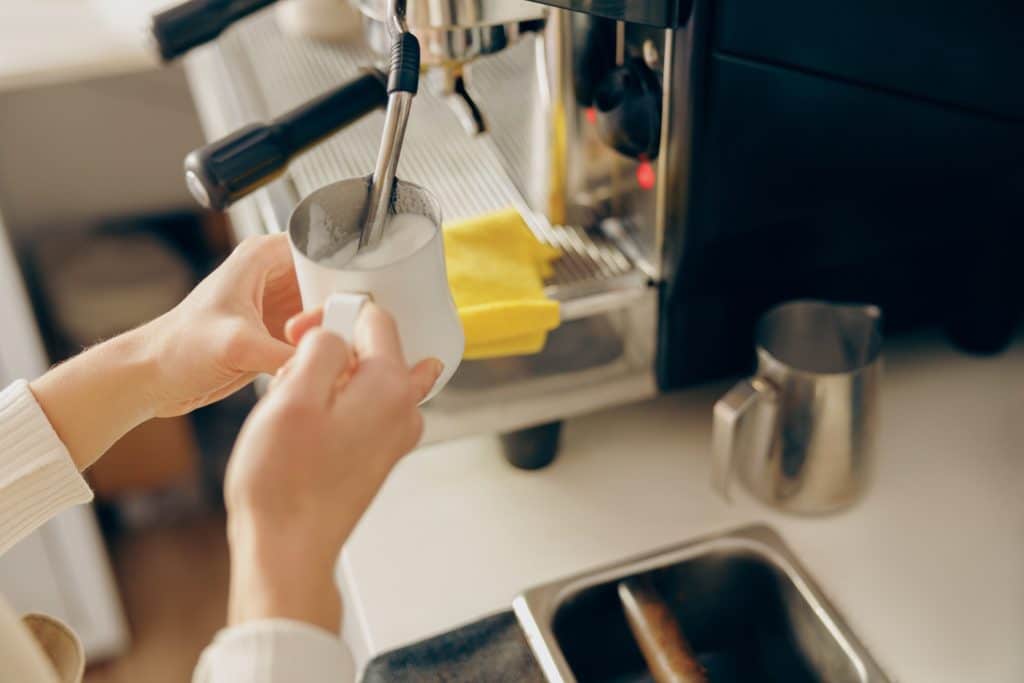 Close-up van twee handen die melk opschuimen met espresso apparaat | Koffiezetapparaat schoonmaken | Asenso Schoonmaakdiensten