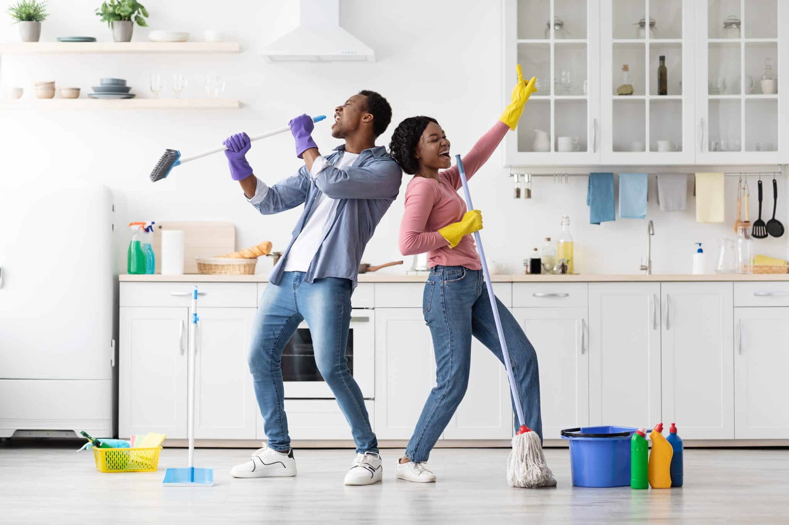 Vrolijk koppel dat doet alsof ze karaoke zingen met schoonmaakspullen in de keuken | Minimalistisch Schoonmaken | Asenso Schoonmaakdiensten