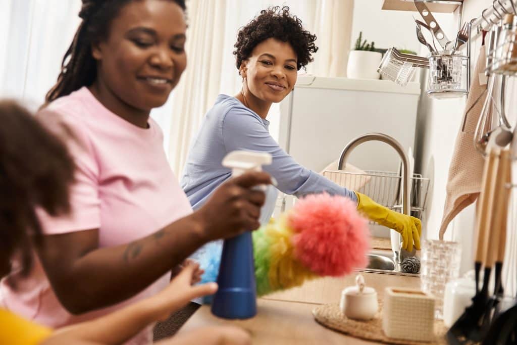 Gezin dat vrolijk de keuken schoonmaakt, twee vrouwen met kind | Minimalistisch Schoonmaken | Asenso Schoonmaakdiensten