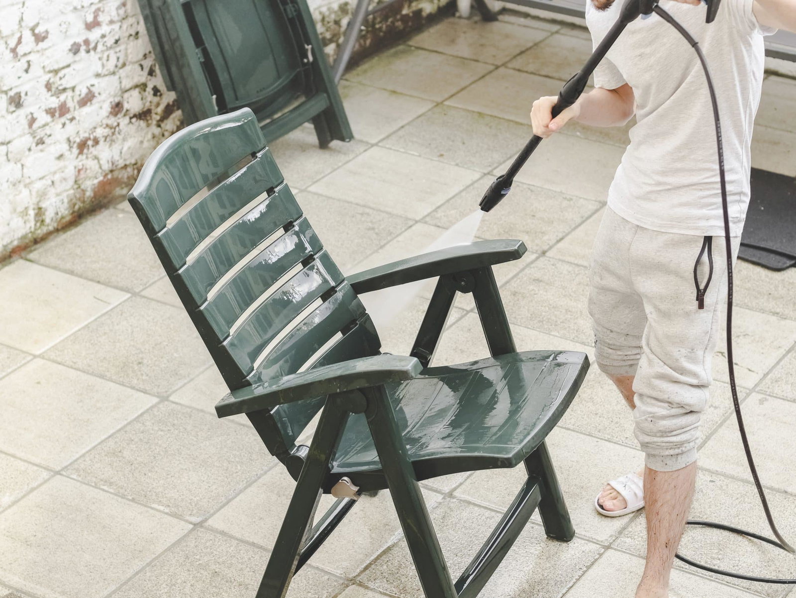 Man in witte outfit die groene plastic tuinstoel schoonmaakt met hogedrukspuit | Tuinmeubelen schoonmaken | Asenso Schoonmaakdiensten