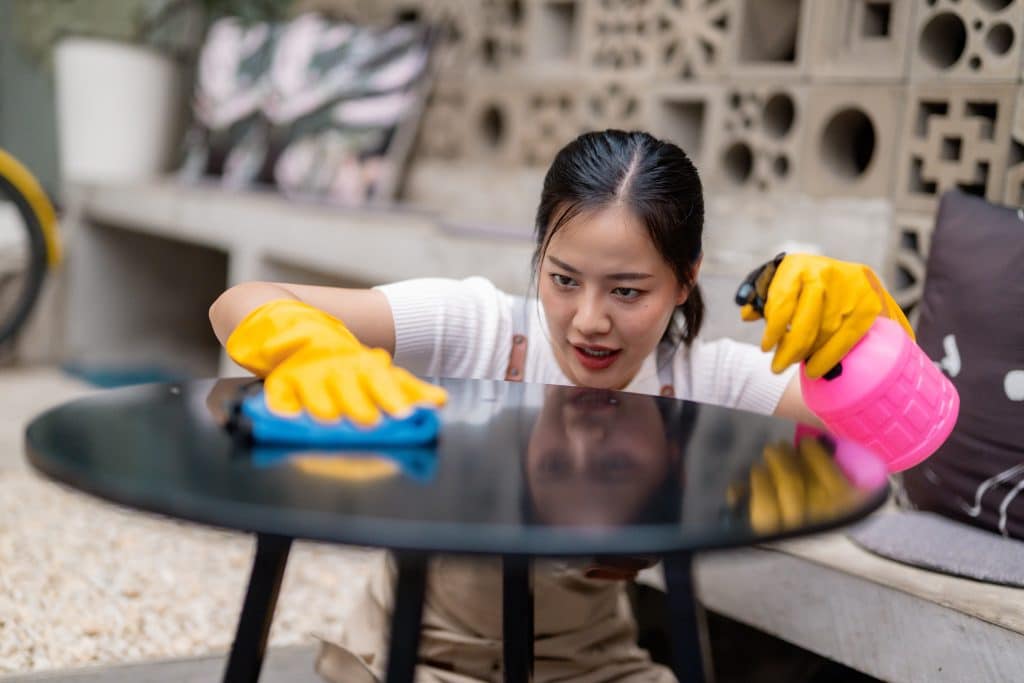 Aziatische vrouw die tuinmeubelen met vochtige doek schoonmaakt | Tuinmeubelen schoonmaken | Asenso Schoonmaakdiensten