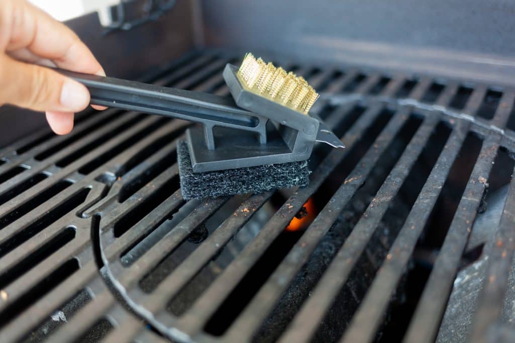 Close-up van hand die met een schraper de barbecue schoonmaakt, de aangekoekte resten | Barbecue schoonmaken | Asenso Schoonmaakdiensten