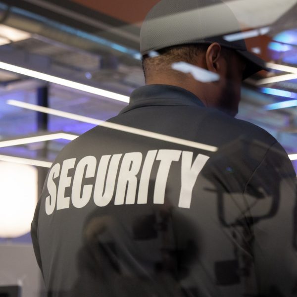 A security guard standing inside a commercial building nearby the window reflecting light